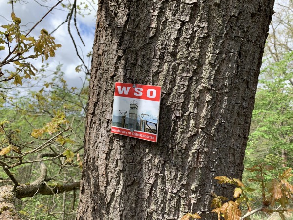 An einem Baumstamm hngt ein Hinweisschild zum Wanderweg zu Schicksalsorten. Auf dem Bild ein Grenzturm der innerdeutschen Grenze