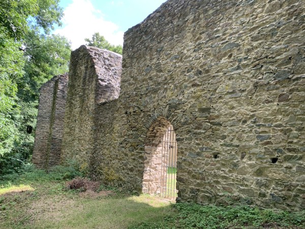 Hohe Mauer mit vergittertem Durchgang und halboffene Fenster