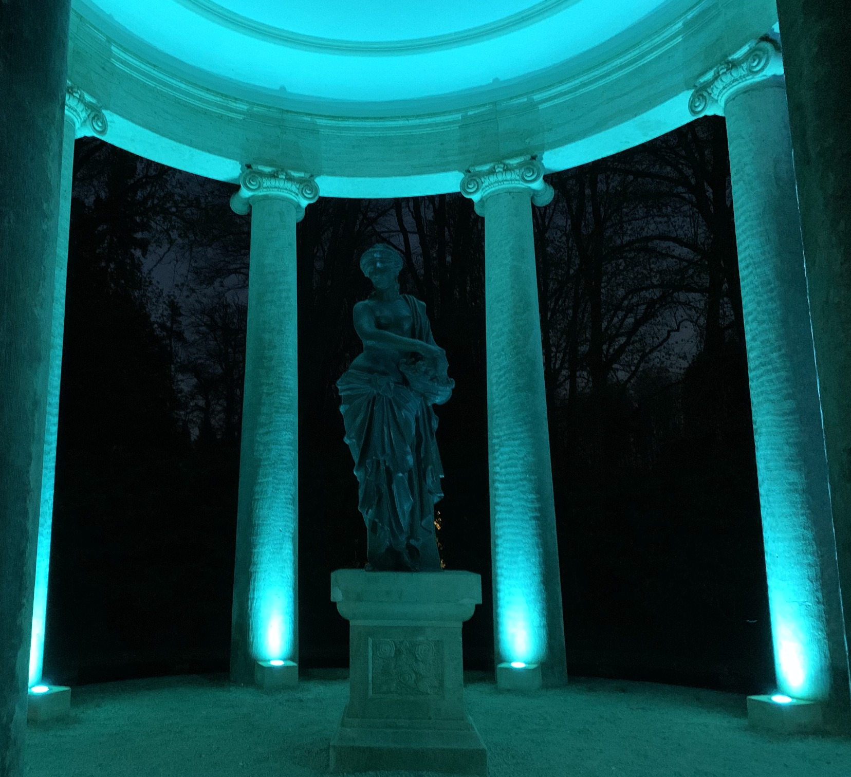 Statue türkisblau angeleuchtet vor Säulen. Dahinter die Nacht.