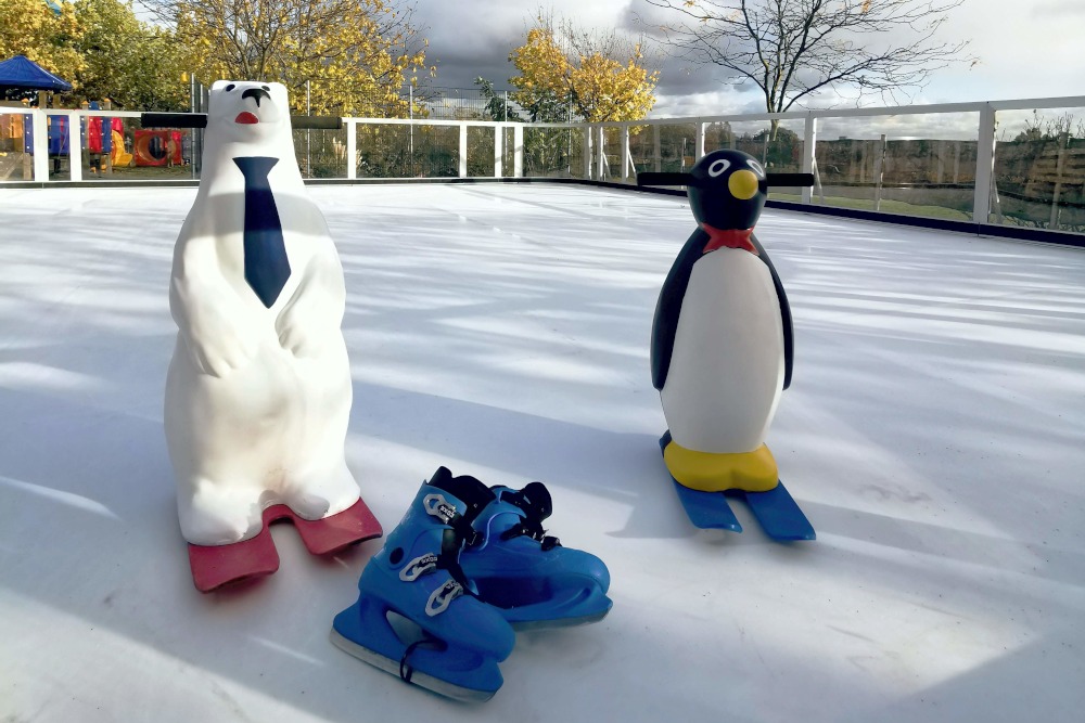 Eisbr und Pinguin mit Skiern auf der Eisbahn. Im Vordergrund ein Paar blaue Schlittschuhe.