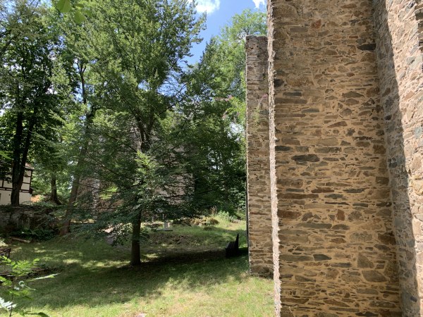 Links: durch Bume Ruine durchschimmernd - rechts hohe Steinmauer bis nach oben