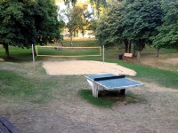 Tischtennisplatte vor Beachvolleyballplatz zwichen ausgetrockneter Wiese und Bumen