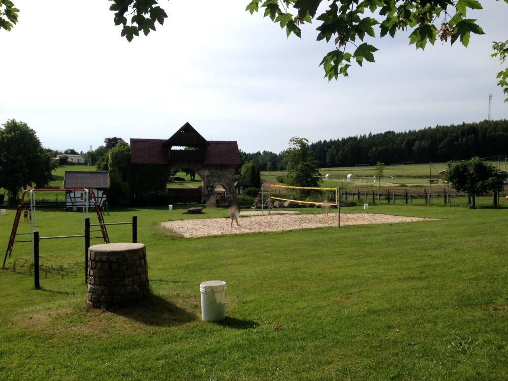 Beachvolleyballplatz in Wiese. Dahinter kleines Gebude. Bume am Horizont.