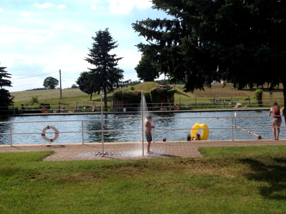 Schwimmbecken zwischen Wiede und Felder und Bume. Junge duscht sich.