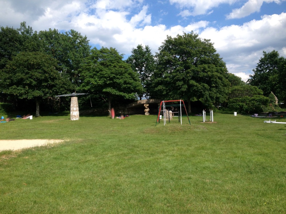 Wiese, darauf Klettergerte, dahinter Bume, blauer Himmel mit Wolken