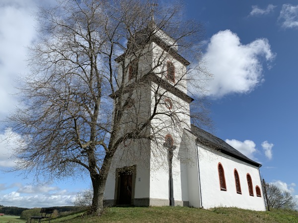 Baum vor Kapelle unter blauem Himmel mit Wolken auf Wiese