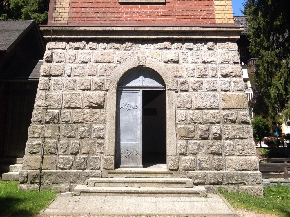 Unter Teil eines Turmes mit halboffener Eingangstr. Von oben ragen Zweige in das Bild