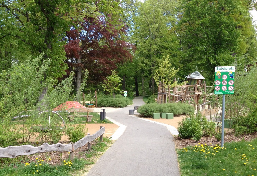 Spielplatz zwischen grnenden Bumen. Ein Weg fhrt hindurch.