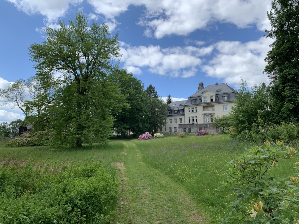 Malerische Wolken und Wiese. Links Bume, rechts ein Herrenhaus