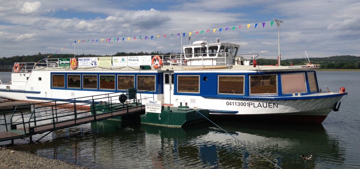 blau weipes Schiff auf Wasser am Steg mit bunten Wimpeln und Werbebannern