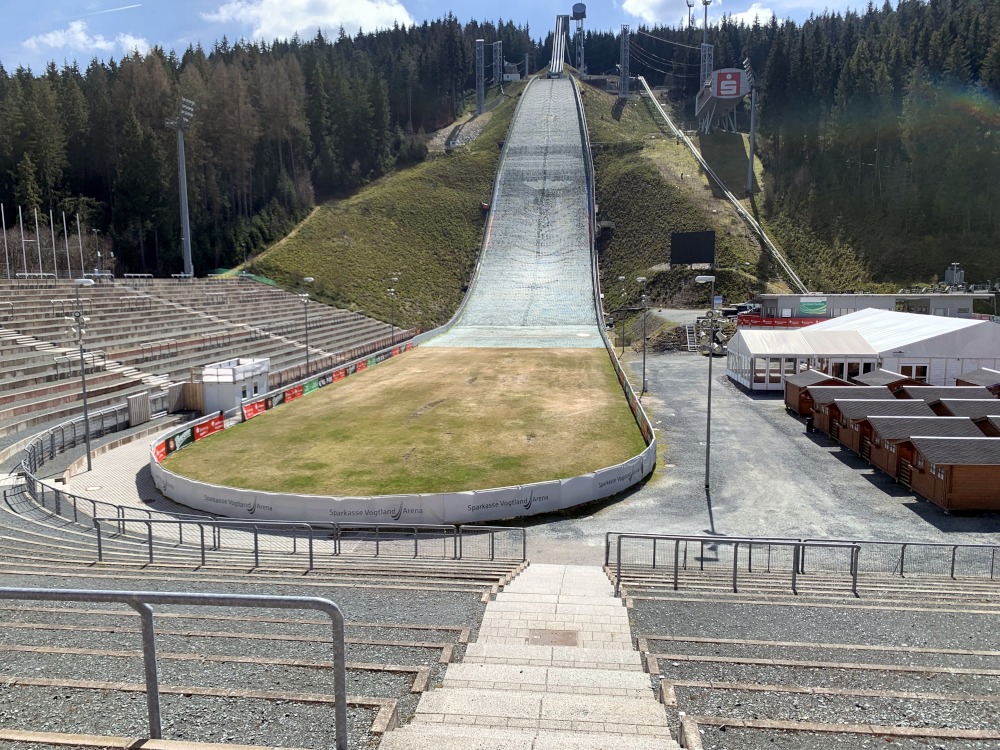 Skisprungschanze am Berg im Wald mit Auslauf, umrahmt von Zuschauer-Sitzplätzen