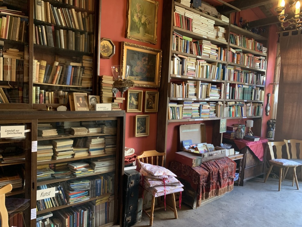 Wand komplett voll mit Regalen und Büchern. In der Mitte zwischen den Regalen alte Gemälde.