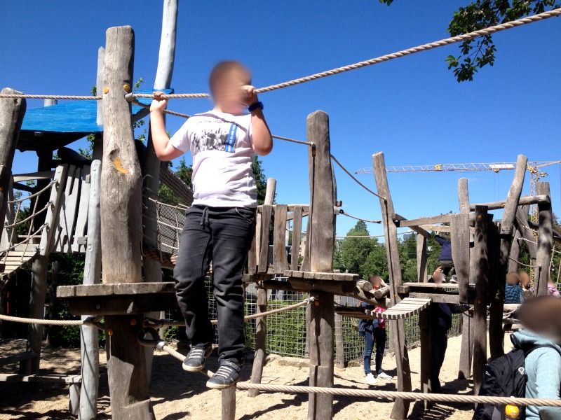 Junge hält sich zwischen 2 Seilen fest. Seile verbinden Holz-Klettergerüst